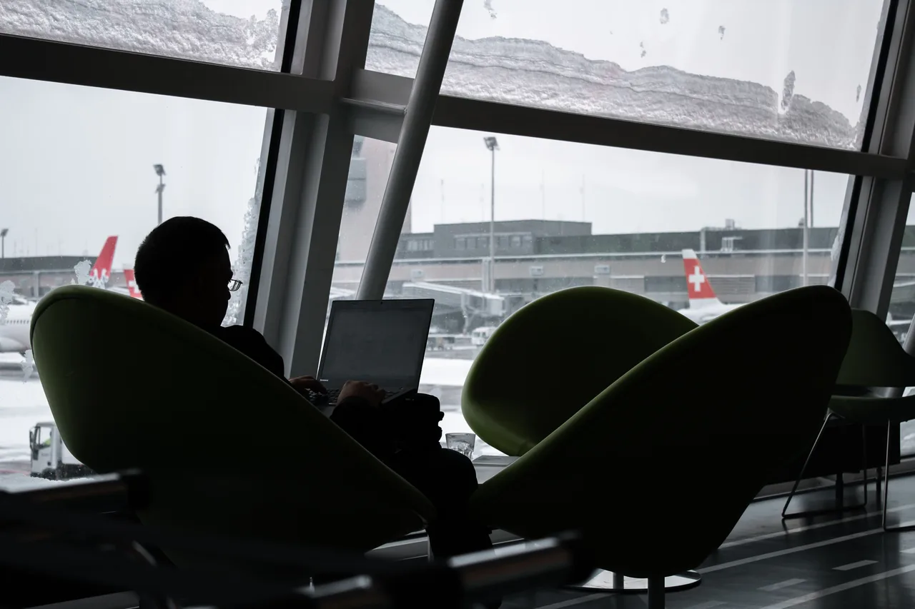Silhouette of a man working on laptop at airport lounge with planes outside