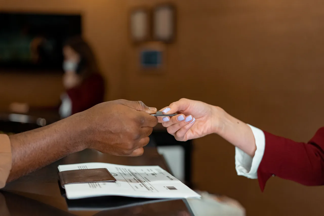 Close-up of a hotel receptionist receiving a credit card from a guest, highlighting a transaction at check-in