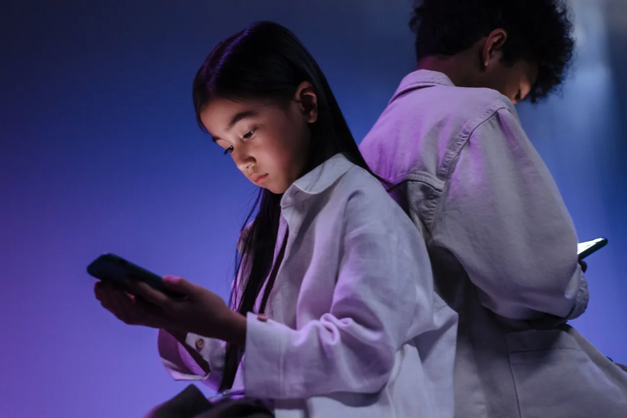 Two children engrossed in using their smartphones in a dimly lit setting