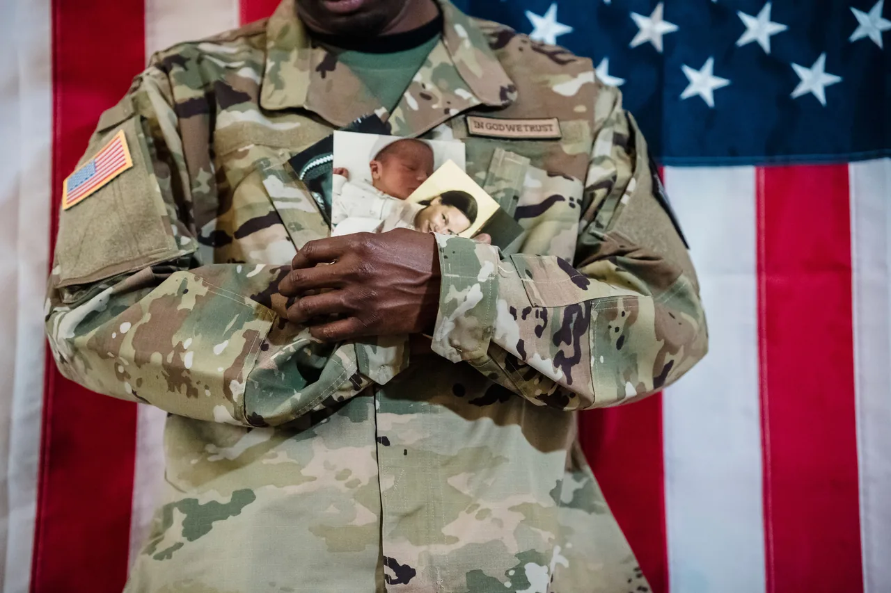 U.S. Army soldier in uniform holding family photos against an American flag backdrop