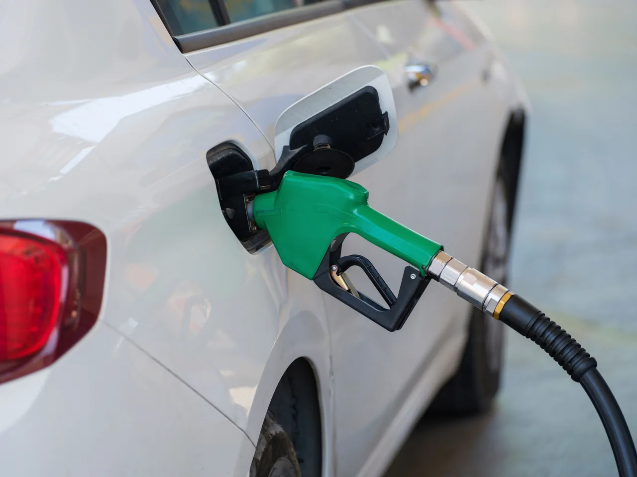 Close-up of a green nozzle refueling a white car at a gas station