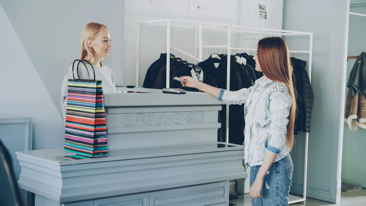 A woman paying by card at a store counter, handing card to female cashier
