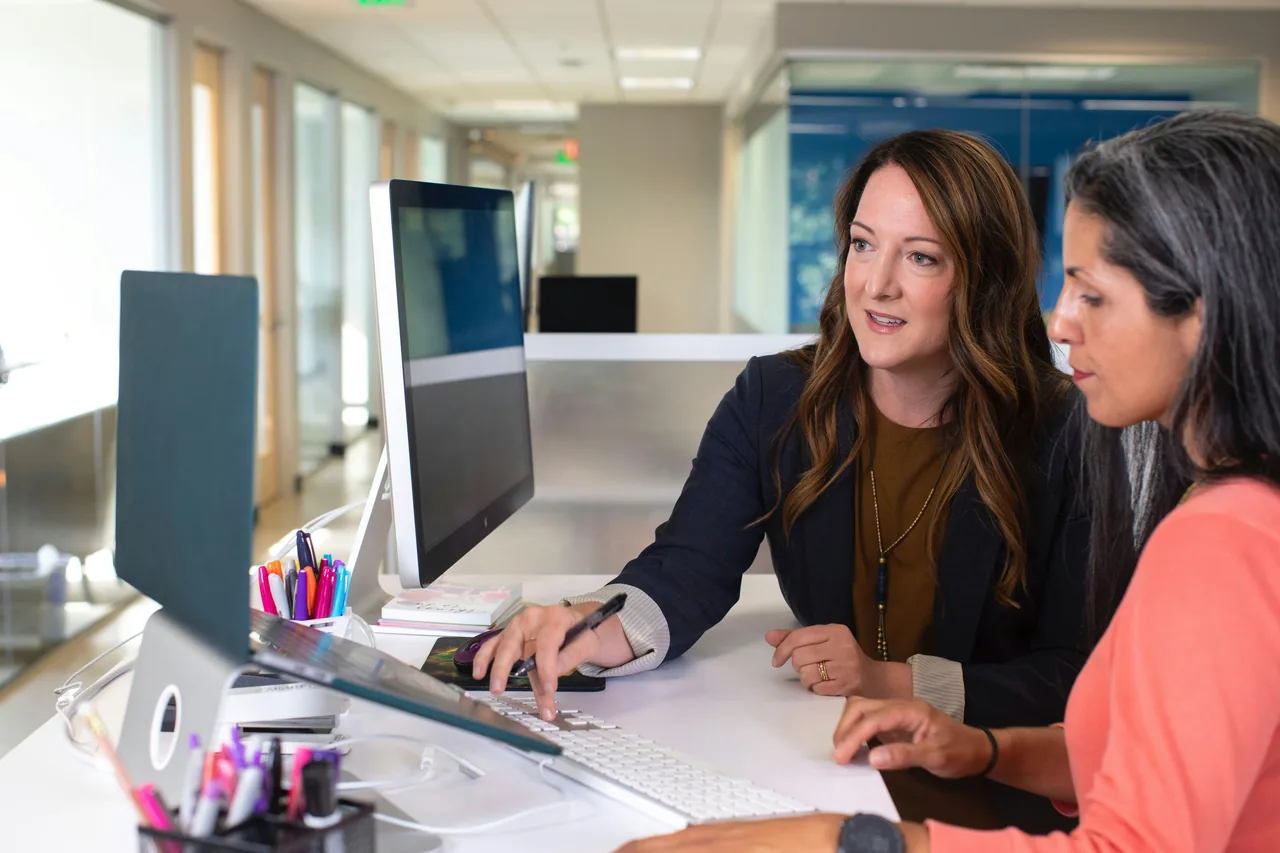 Two business women talking about sales at laptops