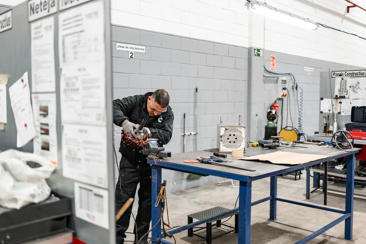 Technician using an angle grinder in a welding zone, generating sparks at a workbench filled with tools and components
